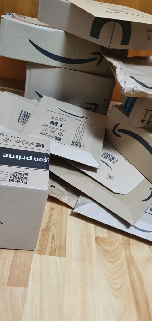 Unsortierter Haufen Amazon-Pakete und -Versandtaschen auf einem Parkettboden
