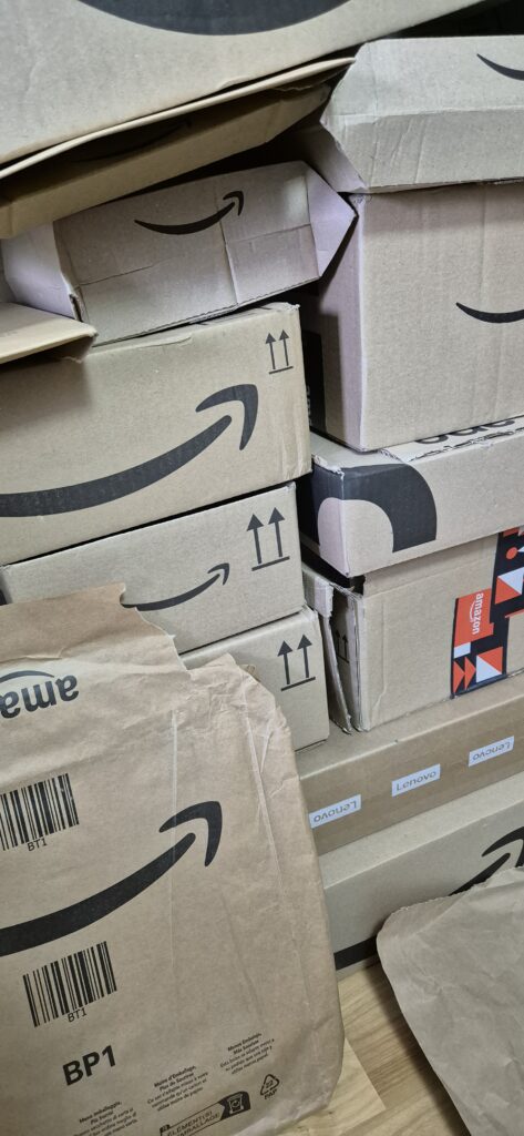 Gestapelte Amazon-Kartons und Papierversandtaschen, dazwischen Lenovo-Verpackungen