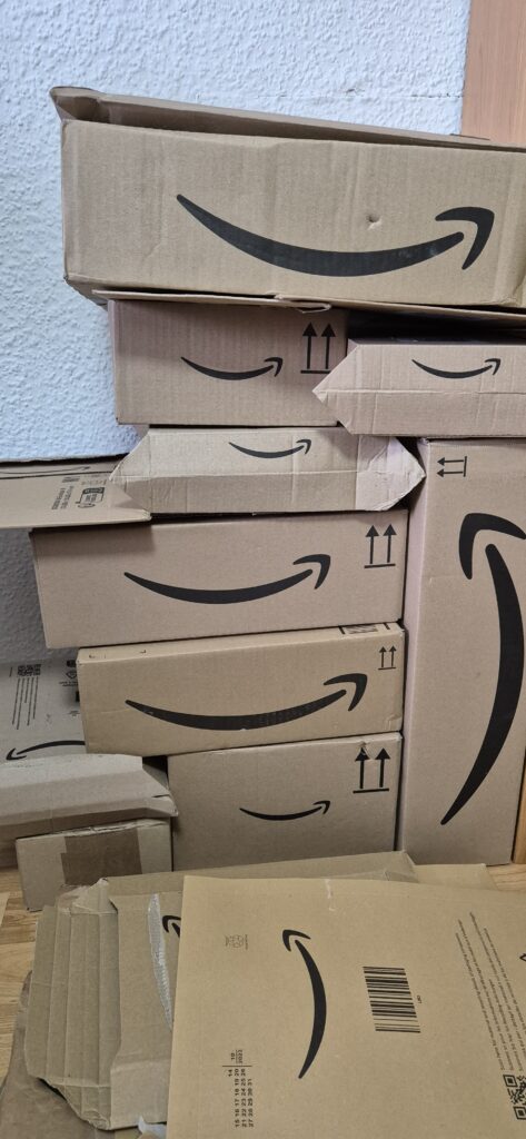 Stapel geöffneter Amazon-Kartons vor einer weiß verputzten Wand