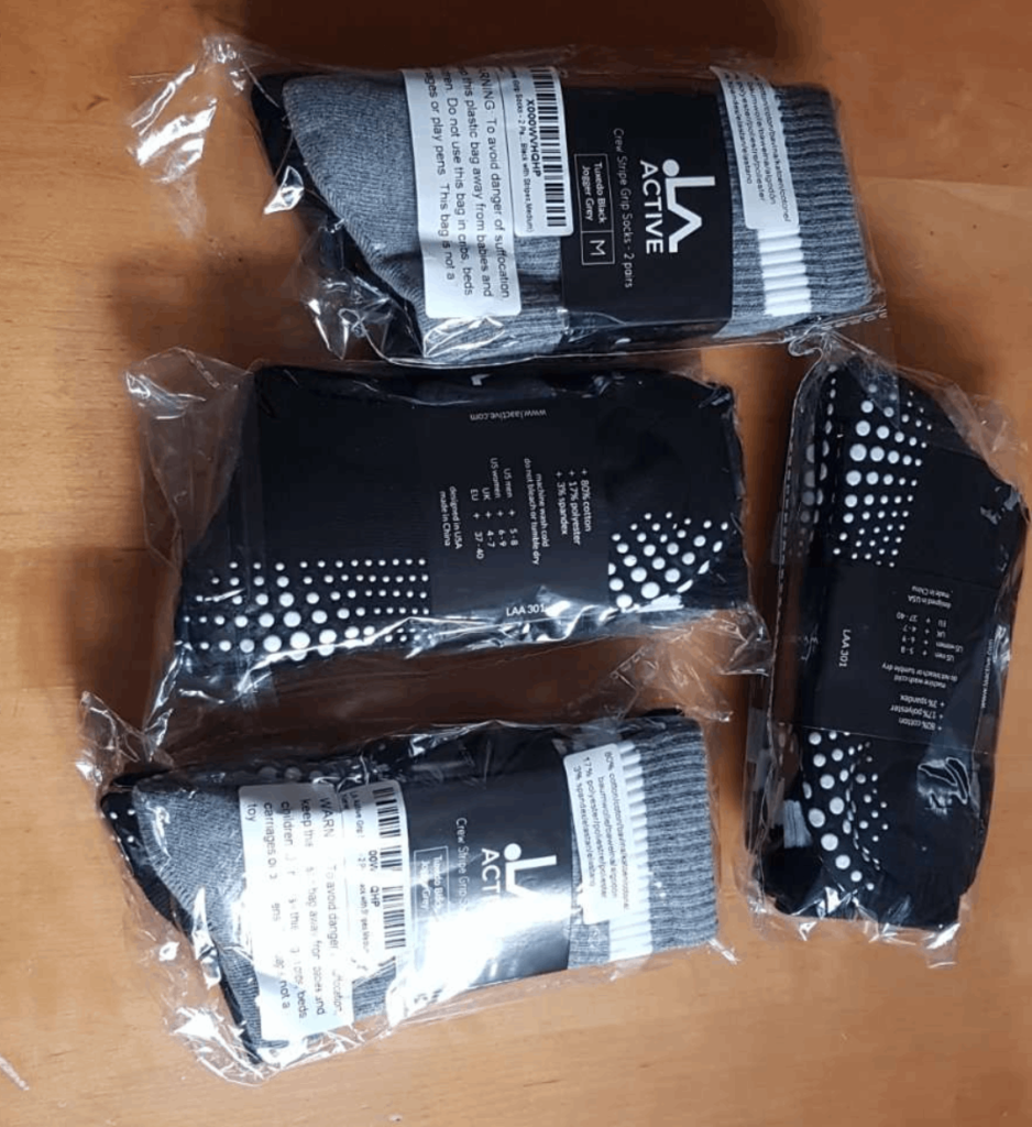 Vier eingeschweißte Paar schwarz-graue Stoppersocken der Marke LA Active auf einem Holztisch