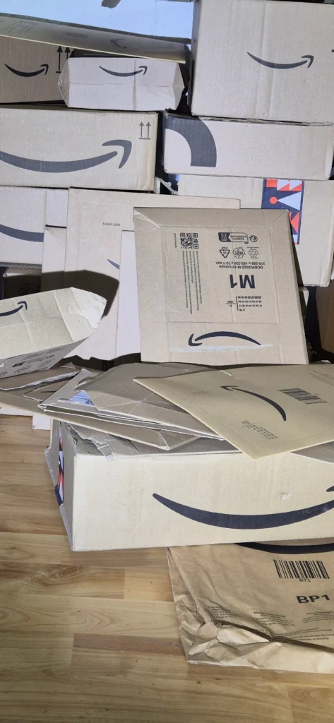 Wand aus gestapelten Amazon-Kartons, davor geöffnete Versandtaschen